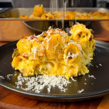 A plated portion of a carbonara pumpkin pasta bake with Parmesan shavings.