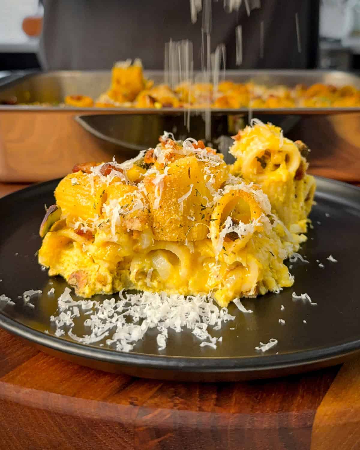 A plated portion of a carbonara pumpkin pasta bake with Parmesan shavings.