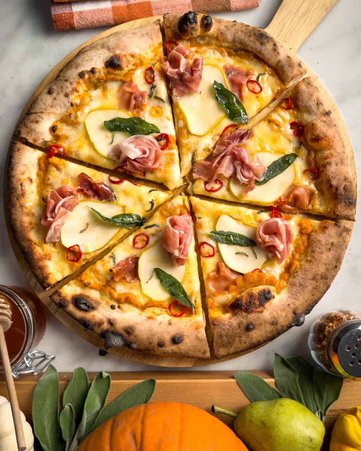 A pumpkin pear pizza with prosciutto, sage, chilis and hot honey sliced into six pieces.