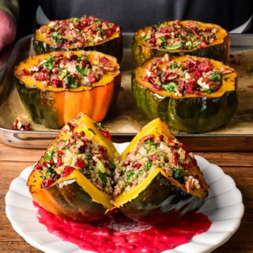 A plated & cut in half turkey quinoa stuffed acorn squash topped with cranberries, pecans, sitting on a swoosh of cranberry puree.