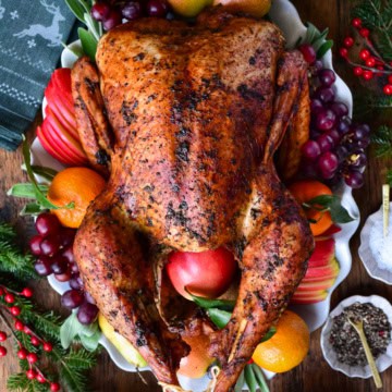 A golden brown garlic and herb roasted turkey on a platter and garnished with fruit and herbs.