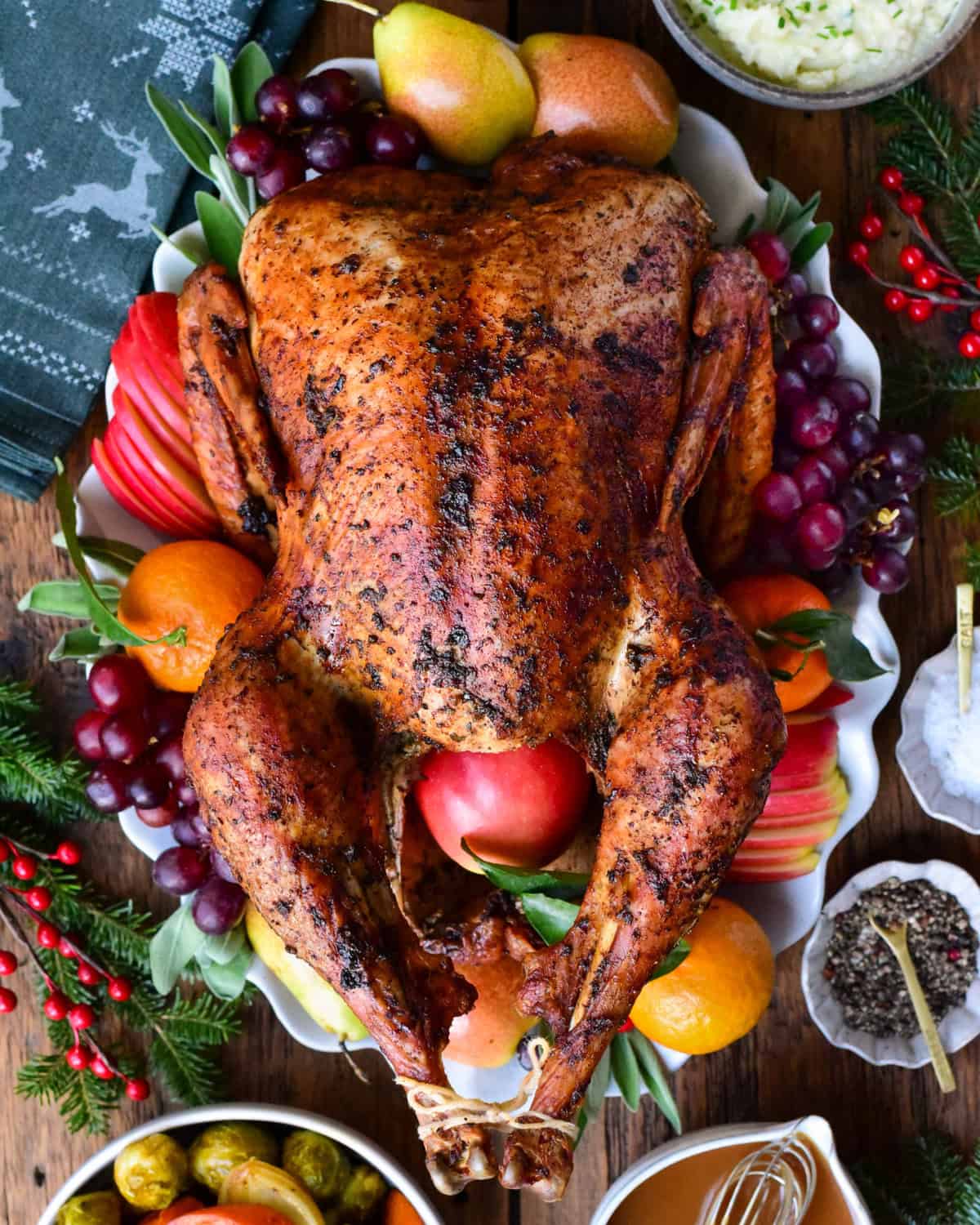 A golden brown garlic and herb roasted turkey on a platter and garnished with fruit and herbs.
