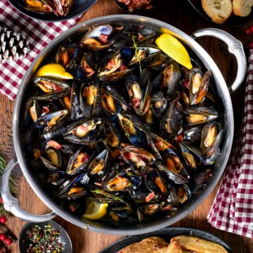A pot of PEI Mussels in Cider Broth with Bacon and Cranberry Salt. they are served bread, lemon wedges and salt and malt vinegar potato wedges.