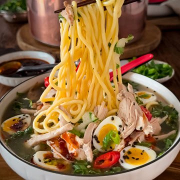 A noodle pull from a bowl of ginger chicken ramen soup with bok choy, ramen-style noodles and jammy quail eggs.