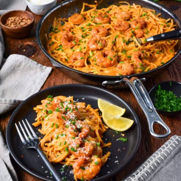 A plate of skillet of creamy spicy Canjun shrimp linguine served with chopped chives and lemon slices.