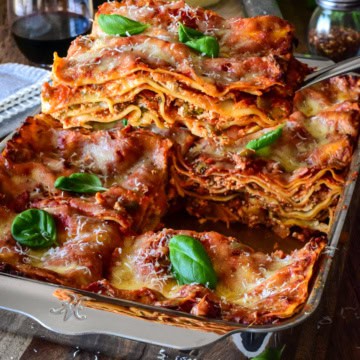 A baking pan with a sausage and beef lasagna and a slice being lifted out to reveal the layers.