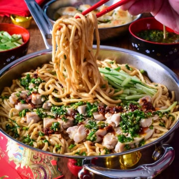 A pan of longevity yi mein noodles with ginger chive chicken, getting pulled up with red chopsticks.