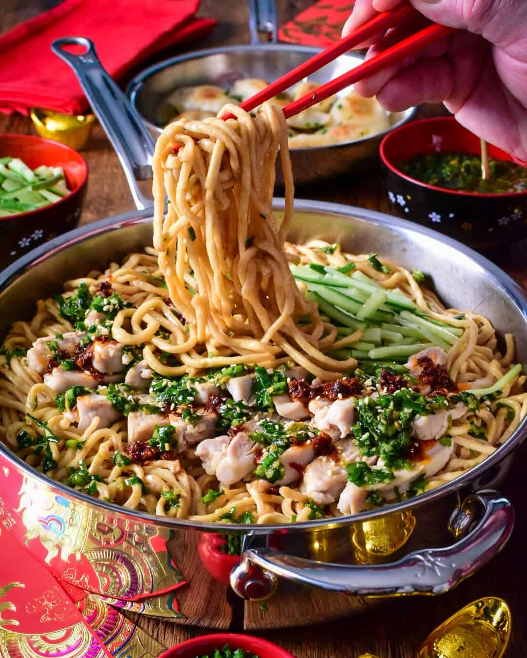 A pan of longevity yi mein noodles with ginger chive chicken, getting pulled up with red chopsticks.