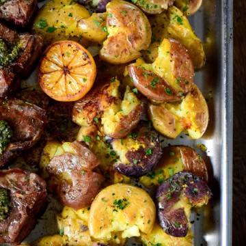Multi coloured smashed baby potatoes served with a charred lemon half and lamb chops.