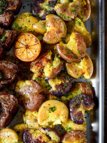 Multi coloured smashed baby potatoes served with a charred lemon half and lamb chops.