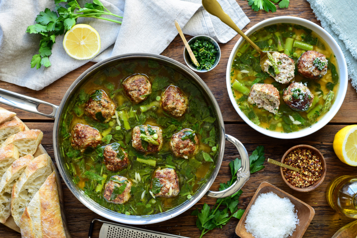 A serving and a pot of chicken ricotta meatballs with lemon orzo brodo, served with grated Parmesan, chili peppers, a lemon-herb gremolata and crusty bread.