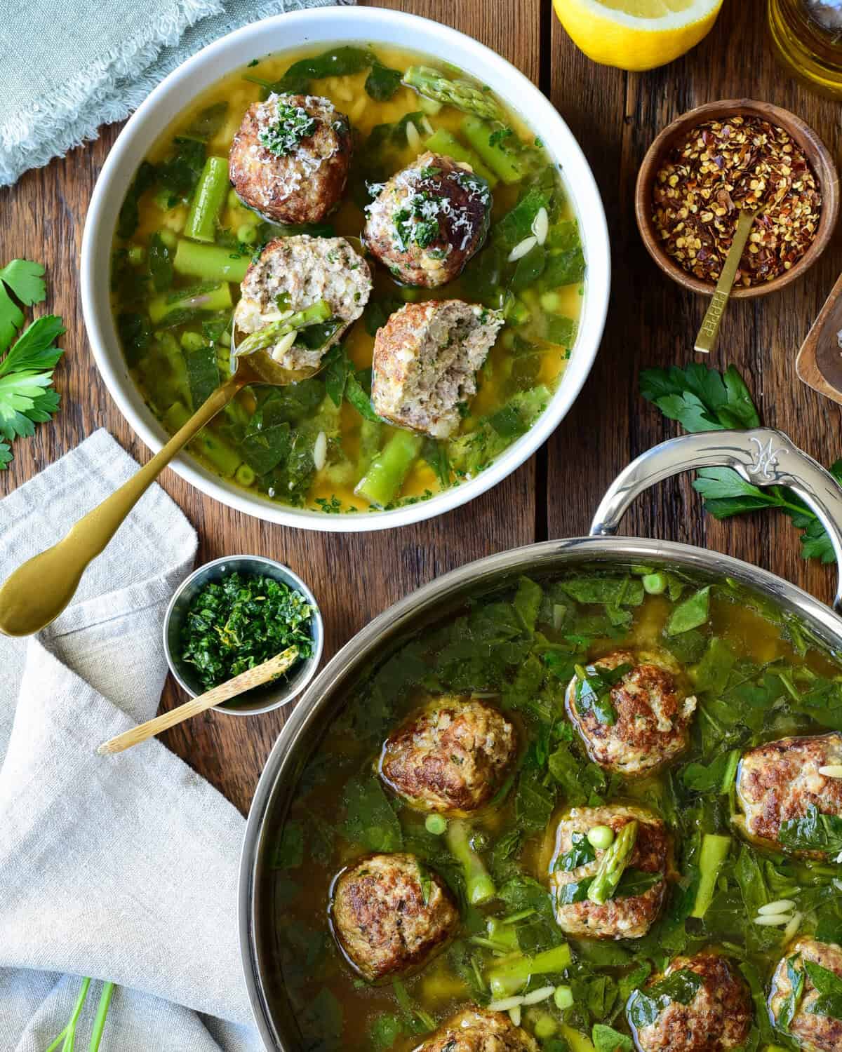 A serving and a pot of chicken ricotta meatballs with lemon orzo brodo, served with grated Parmesan, chili pepper, and a lemon-herb gremolata.