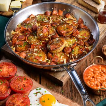 A crispy Irish Pub potato skillet with sausage, bacon and served with sunnyside up eggs, roasted tomatoes and baked beans.