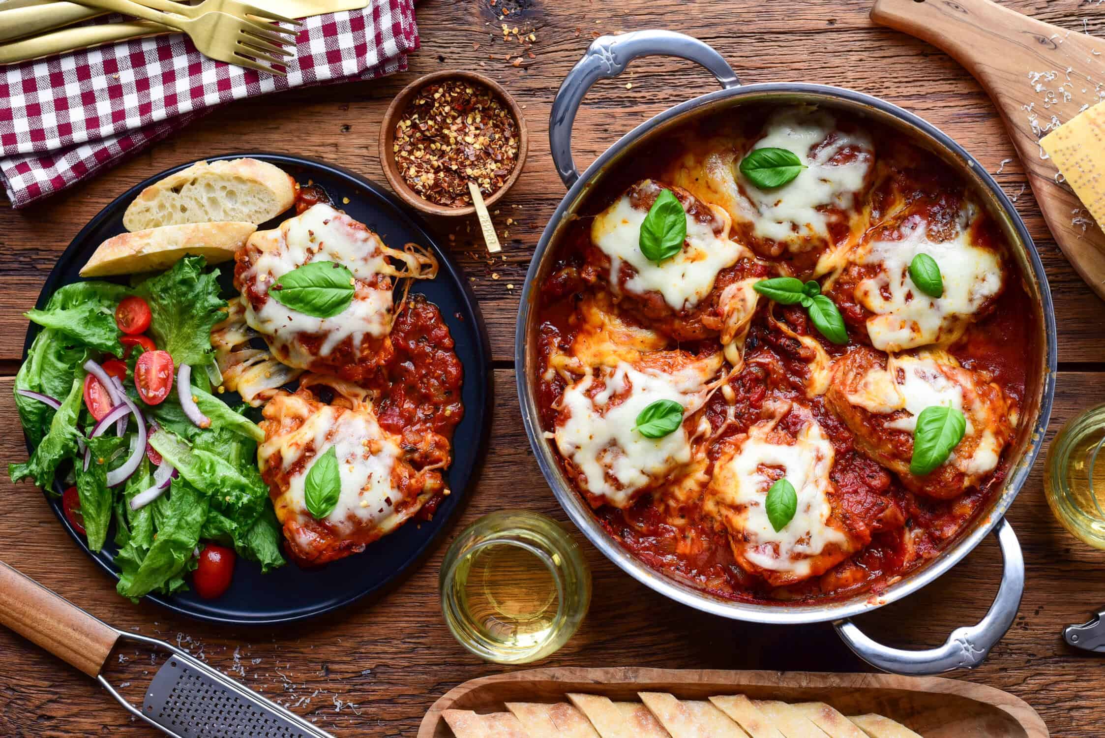 A sauteuse with chicken parm, chicken thighs and a serving with salad and bread for dipping in the sauce.