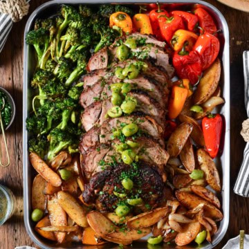 A sliced slow roasted pork butt with crushed olives and parsley. Served on a sheet pan with roasted fingerling potatoes, peppers and broccoli.