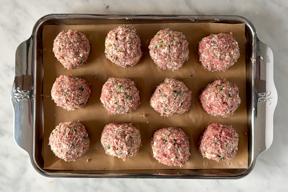 Twelve raw chicken meatballs on a tray.