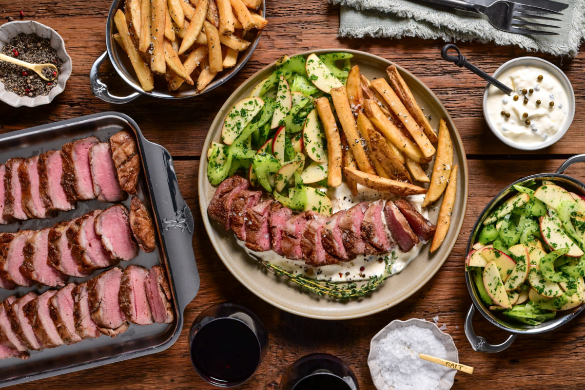 A pan-seared Lamb Sirloin Steak Frites. Paired with tangy green peppercorn labneh, crispy rosemary fries, and a fresh celery-apple salad.