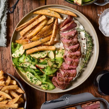 A pan-seared Lamb Sirloin Steak Frites. Paired with tangy green peppercorn labneh, crispy rosemary fries, and a fresh celery-apple salad.