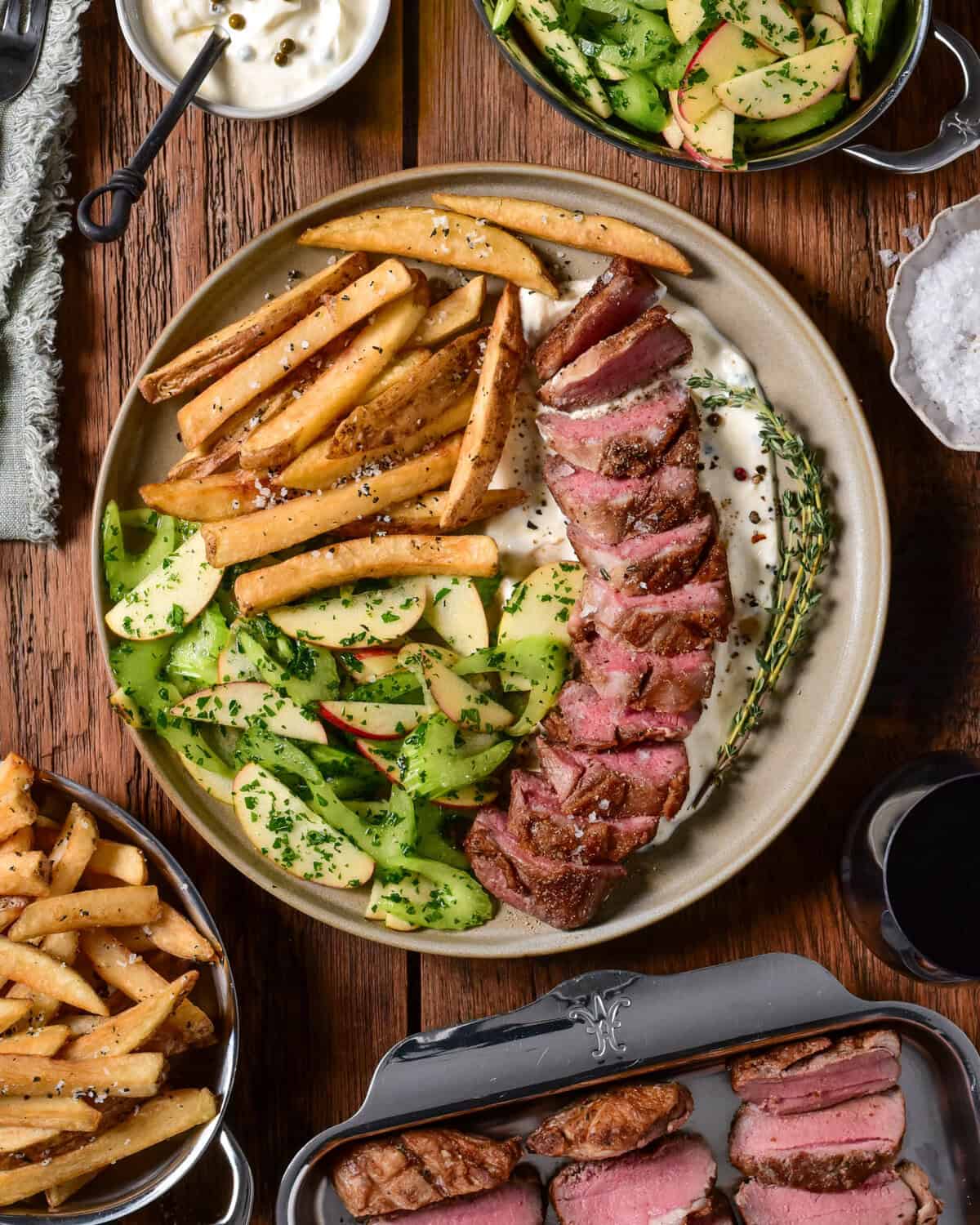 A pan-seared Lamb Sirloin Steak Frites. Paired with tangy green peppercorn labneh, crispy rosemary fries, and a fresh celery-apple salad.