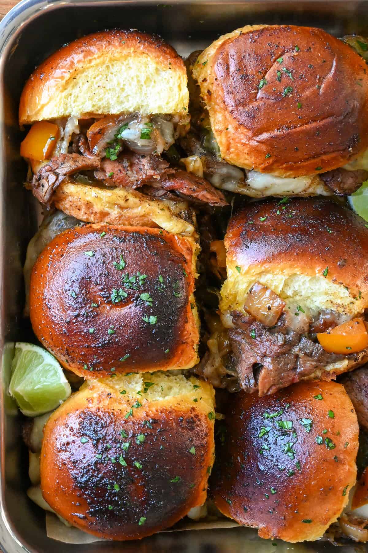 A close-up of six steak sliders in a pan. Some of the sliders are on their sides, revealing the insides.