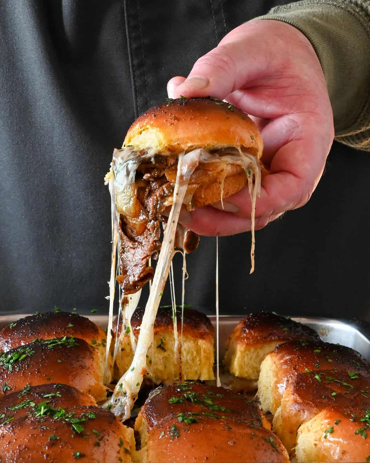 A steak fajita slider is getting lifted out of a pan of sliders with a cheese pull.