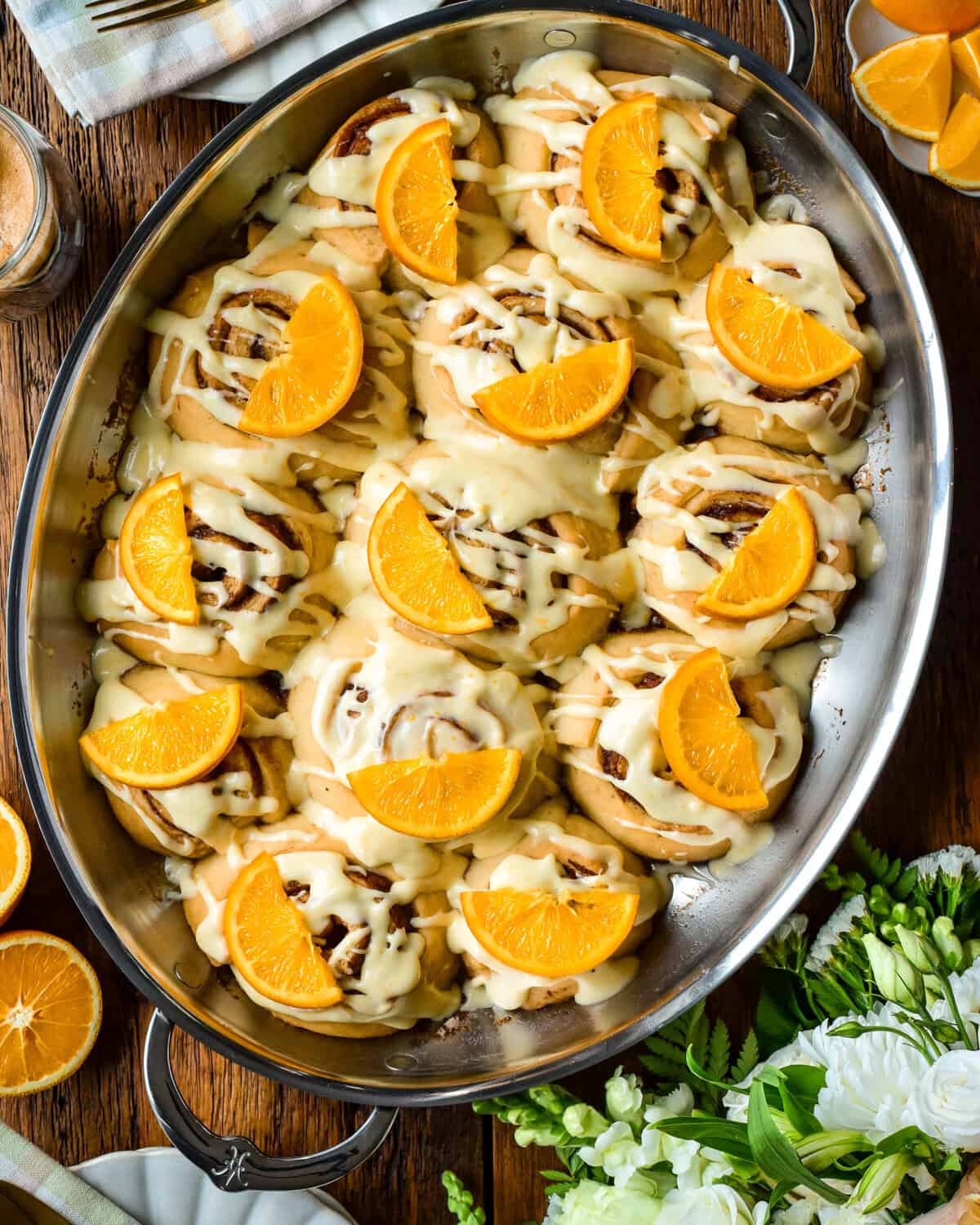 An oval au gratin roaster with orange glazed cinnamon rolls, each topped with a slice of candied orange. 