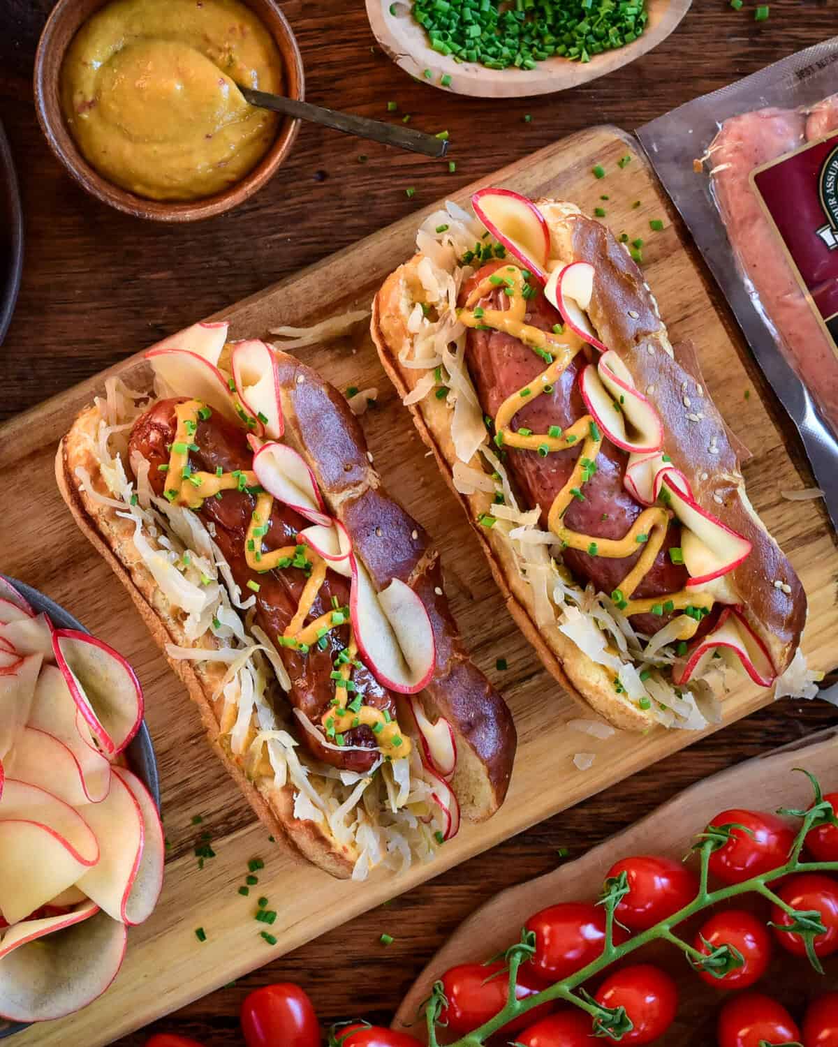 Two charcoal grilled bratwurst with pickled apples, sauerkraut, and mustard on pretzel buns.