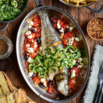 A whole roasted branzino in a fish pan with tomatoes, feta and olives. Served with toasted sourdough, a cucumber slaw and shoestring fries.