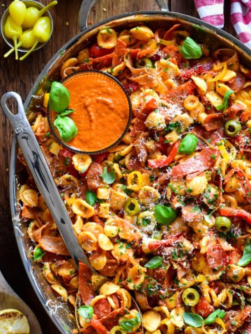 A chopped Italian romesco pasta salad with crispy spicy deli meats in a platter with extra sauce.