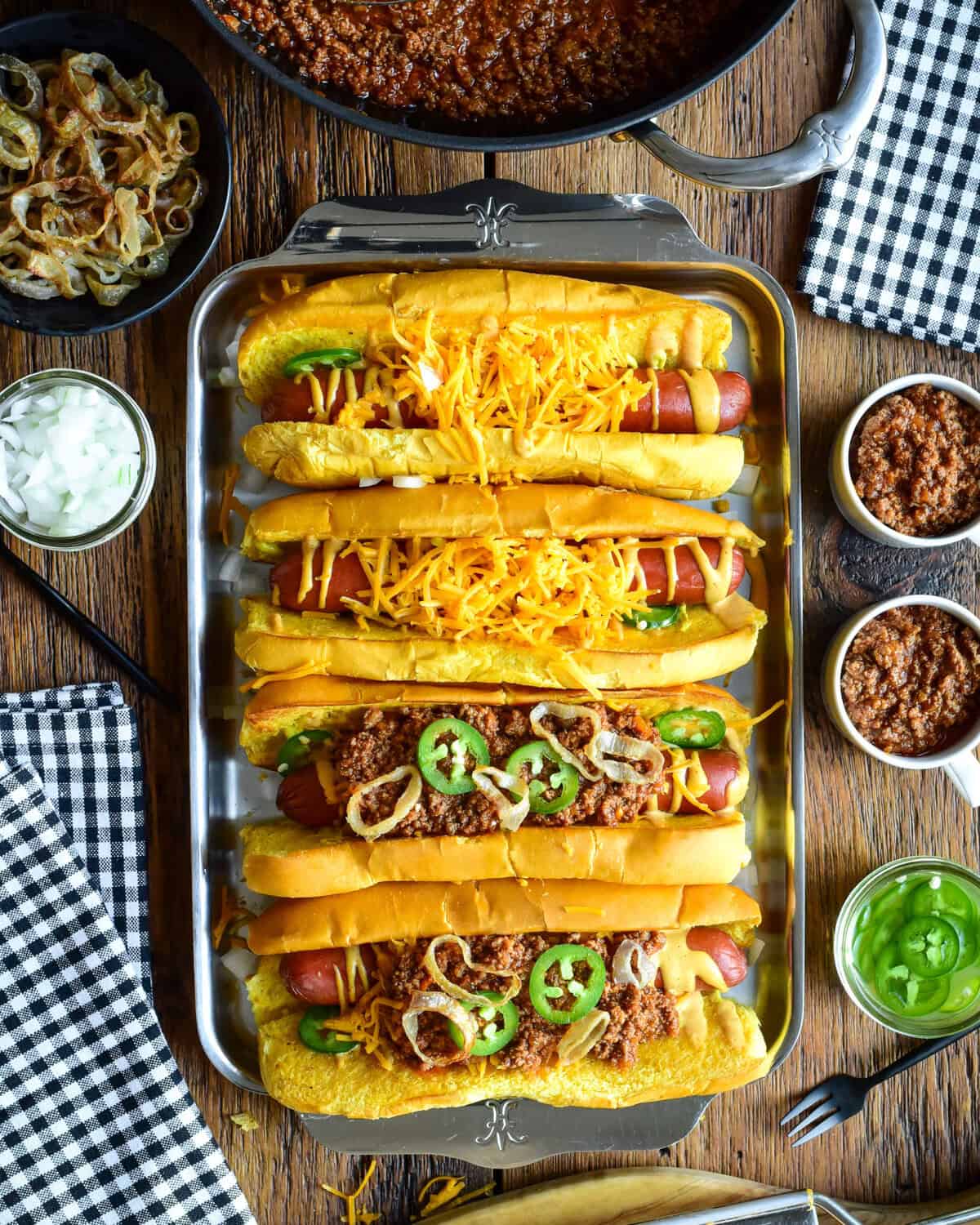 A tray with four chili cheese dogs, two have no chili. The chili is served in small cups to pour over the dogs.