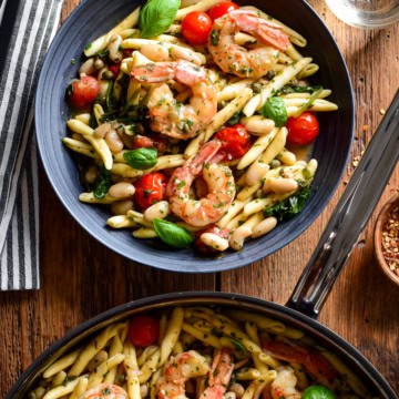 A pan and a bowl with Lemon Caper Shrimp Piccata Pasta with White Beans. This pasta is served with bread, chili flakes white wine an extra fresh basil and tomatoes.
