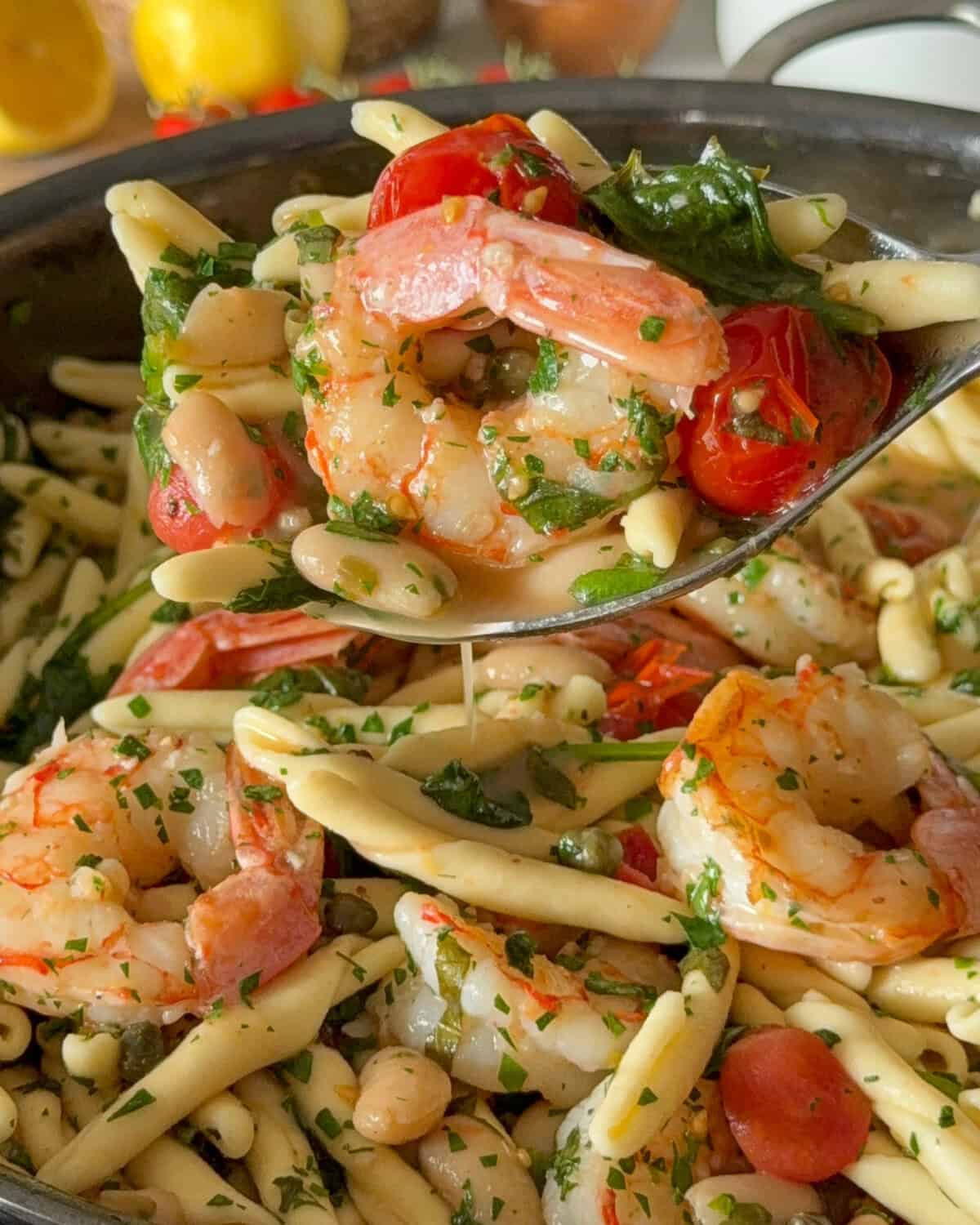 A pan of shrimp piccata pasta with a large serving spoon holding a serving.