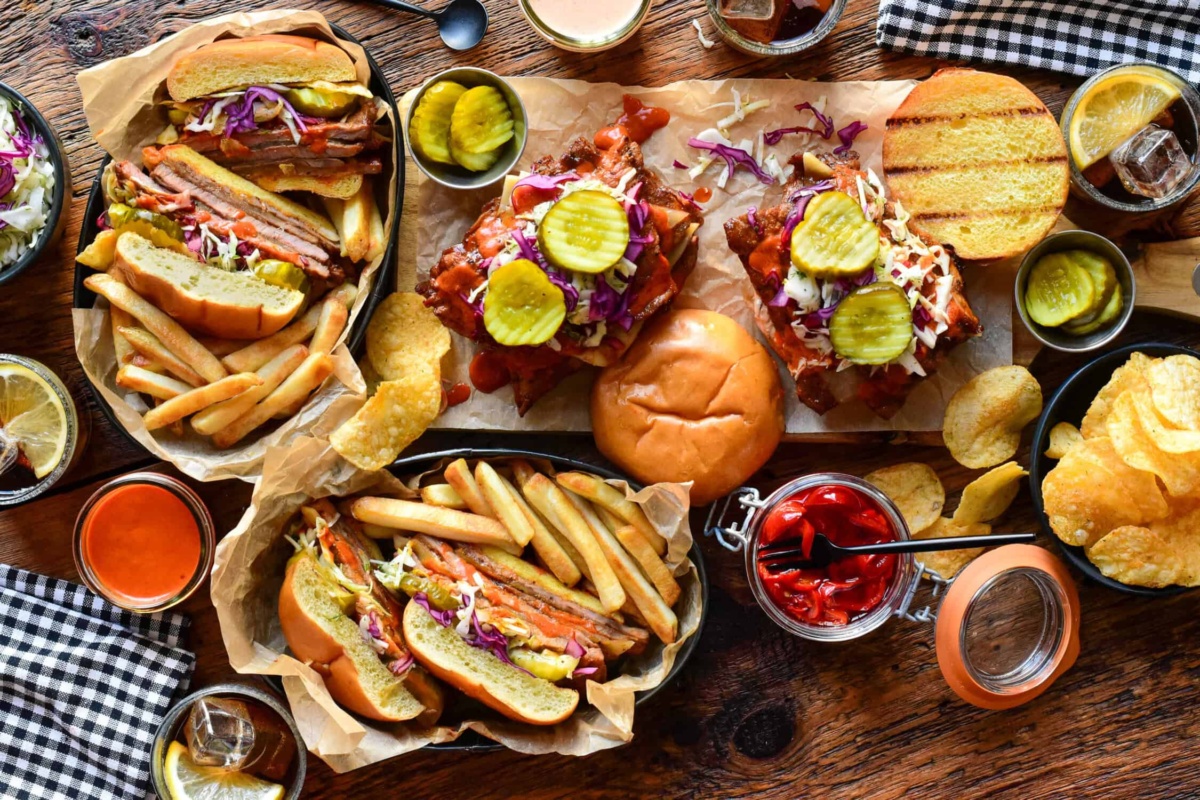 Delicious Nashville hot honey veal cutlet sandwiches with pickles, coleslaw, and side dishes on a rustic wooden table.