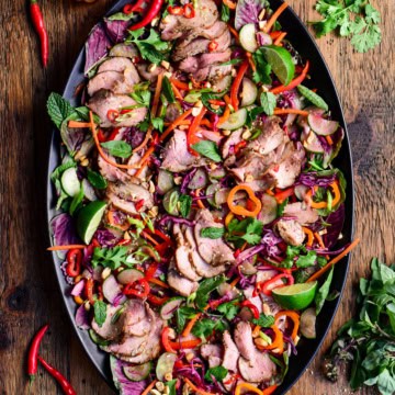 A colourful platter with a Spicy Thai Pork Tenderloin Crunchy Herb Salad. Served with a crispy roasted rice powder, extra herbs and dressing.