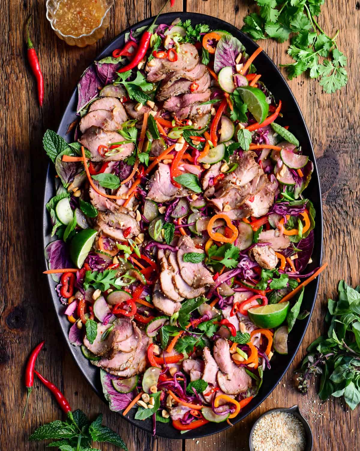 A colourful platter with a Spicy Thai Pork Tenderloin Crunchy Herb Salad. Served with a crispy roasted rice powder, extra herbs and dressing.