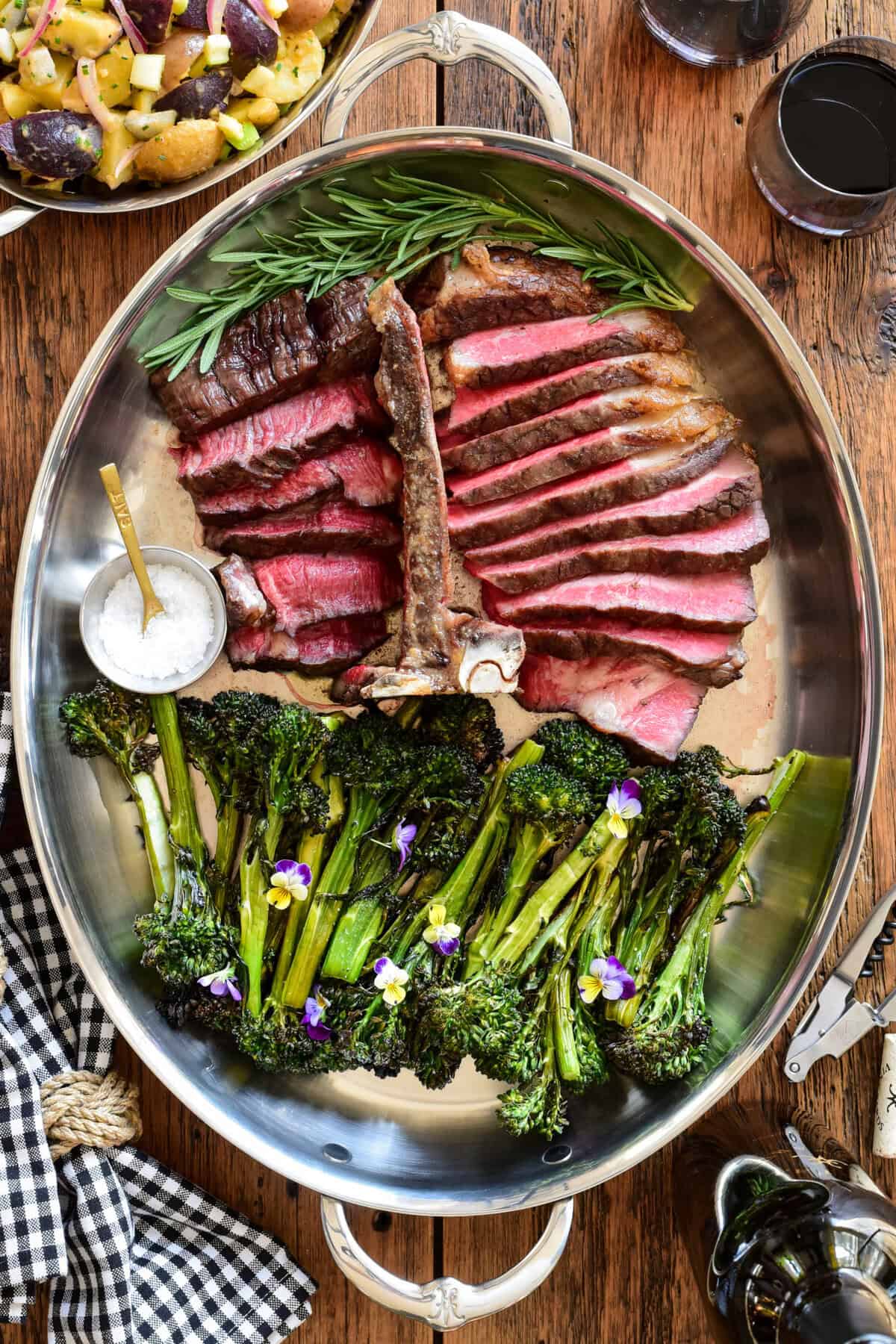 A thick t-bone steak, slice and served in a platter with grilled broccolini, fresh herbs and finishing salt.