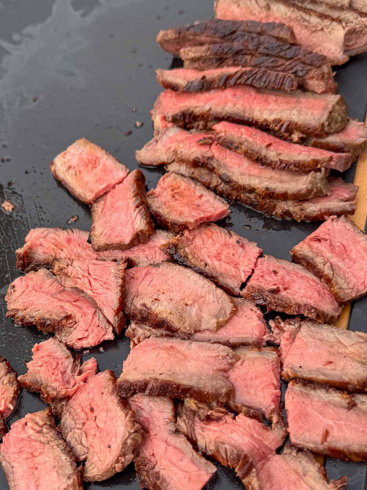 A cutting board of medium-rare striploin steak slices for a Chimichurri Steak Flatbread recipe.