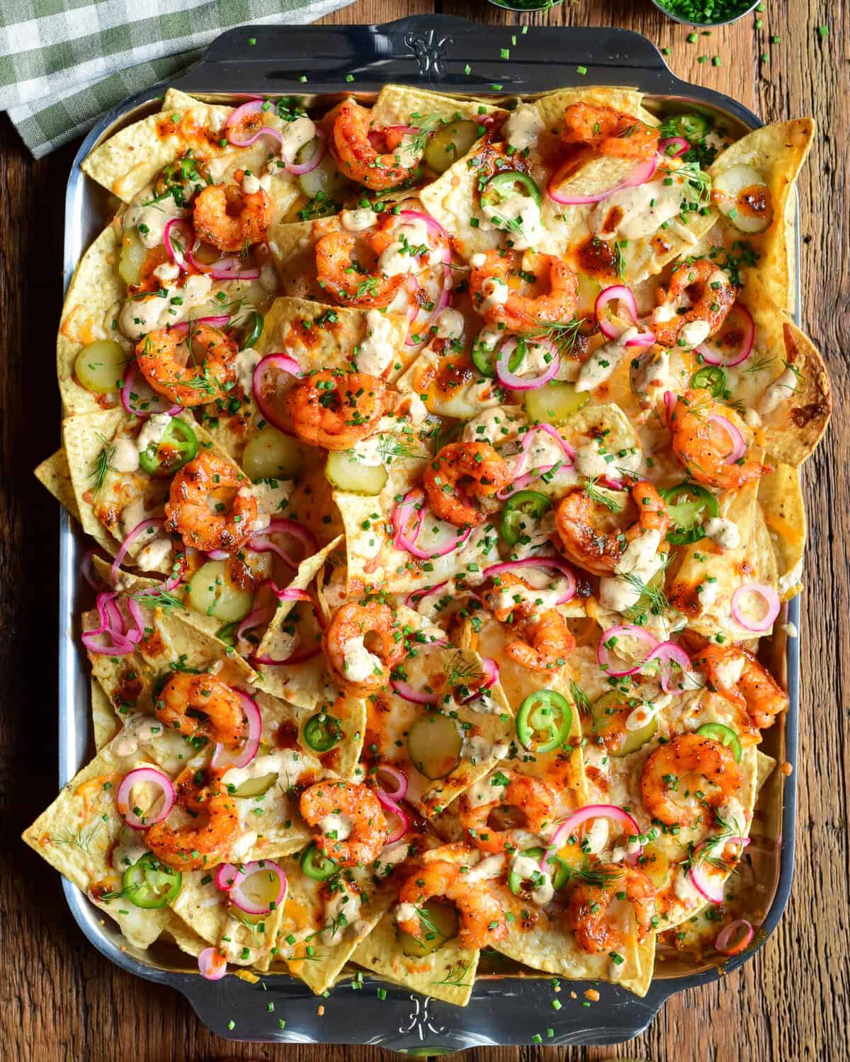 A tray of Nashville Hot Honey Shrimp Nachos with Pickle Crema. Layered with pickled onions, jalapenos, dill pickle slices and herbs.