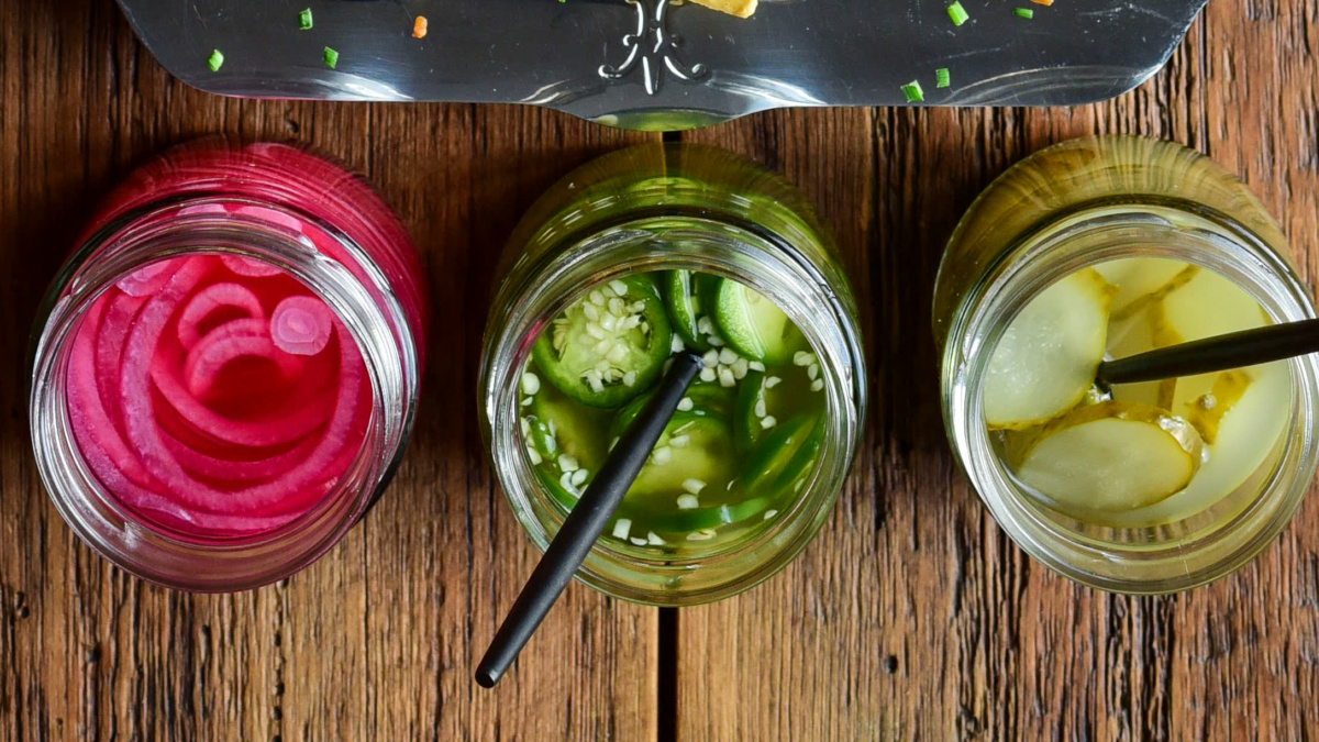 Three jars of pickles; one red onion, one jalapeno and one regular pickle slices.