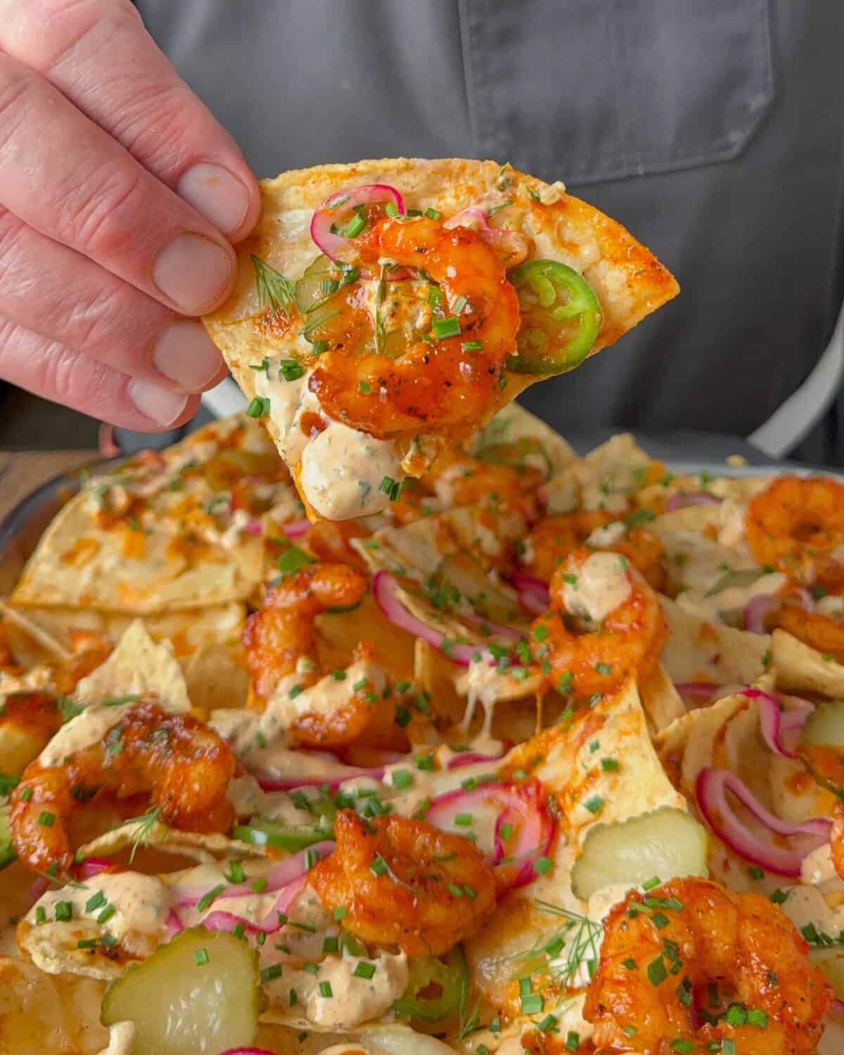 A close up of a loaded shrimp nacho being held up.
