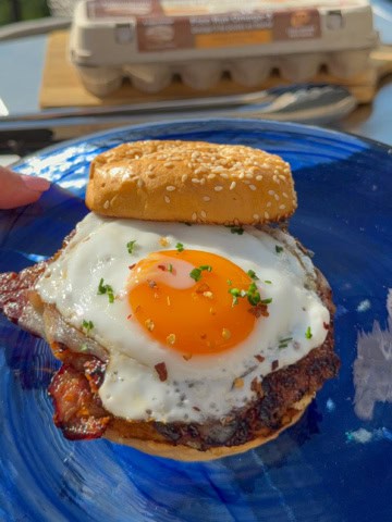 A sausage and sunny-side egg breakfast smash burger on a blue glass plate.