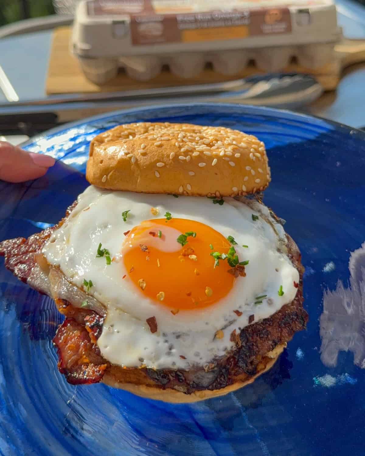 A sausage and sunny-side egg breakfast smash burger on a blue glass plate.