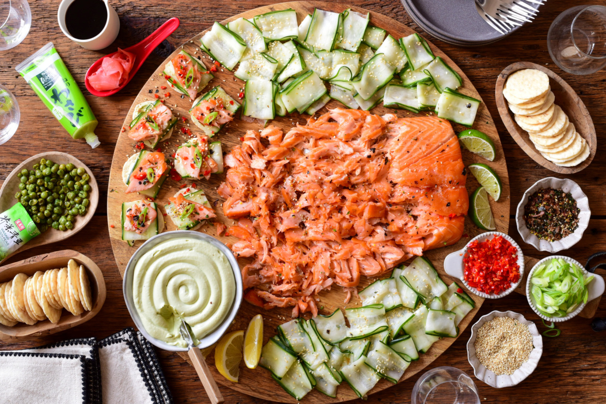 A Smoked Salmon Board with Avocado Lime Cream Cheese served on a round board with extra toppings surrounding it.