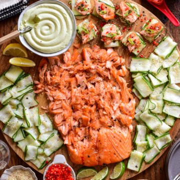 A Smoked Salmon Board with Avocado Lime Cream Cheese served on a round board with extra toppings surrounding it.