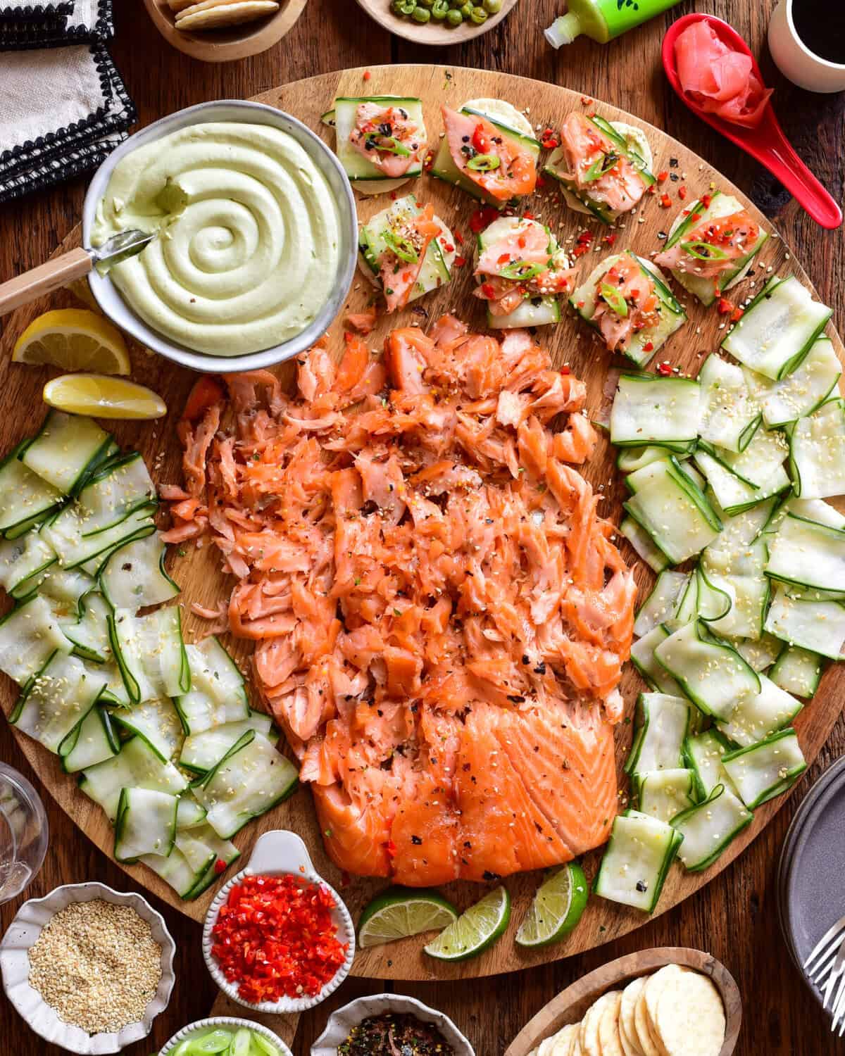 A Smoked Salmon Board with Avocado Lime Cream Cheese served on a round board with extra toppings surrounding it. 