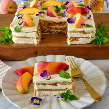 Delicious layered icebox cake with caramelized peaches, mascarpone cream, and edible flowers, served on a white plate with a slice cut out.
