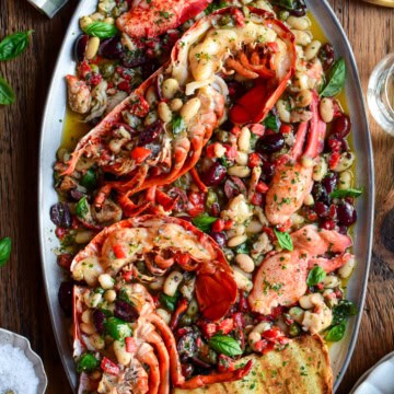 A colourful platter with charcoal-grilled lobster halves over a warm Mediterranean garlic oil with beans, capers, olives, red peppers and herbs. It is served with toasted sourdough slices.