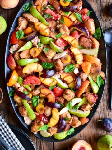 Colorful late summer stone fruit panzanella salad with fresh basil on a black platter, featuring peaches, plums, and tomatoes, perfect for seasonal dining.