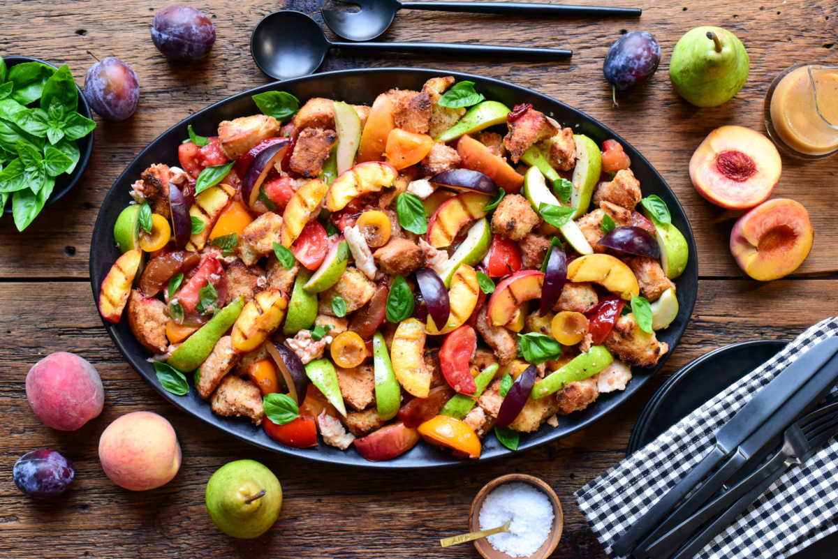 Colorful late summer stone fruit panzanella salad with fresh peaches, plums, and basil on a rustic wooden table, perfect for seasonal dining.
