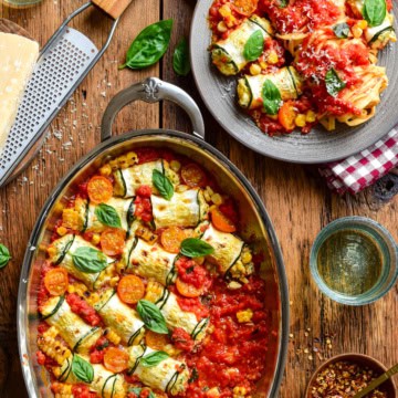 Delicious summer zucchini involtini filled with ricotta and corn, baked in a tomato sauce, garnished with fresh basil leaves, served with a side of pasta.